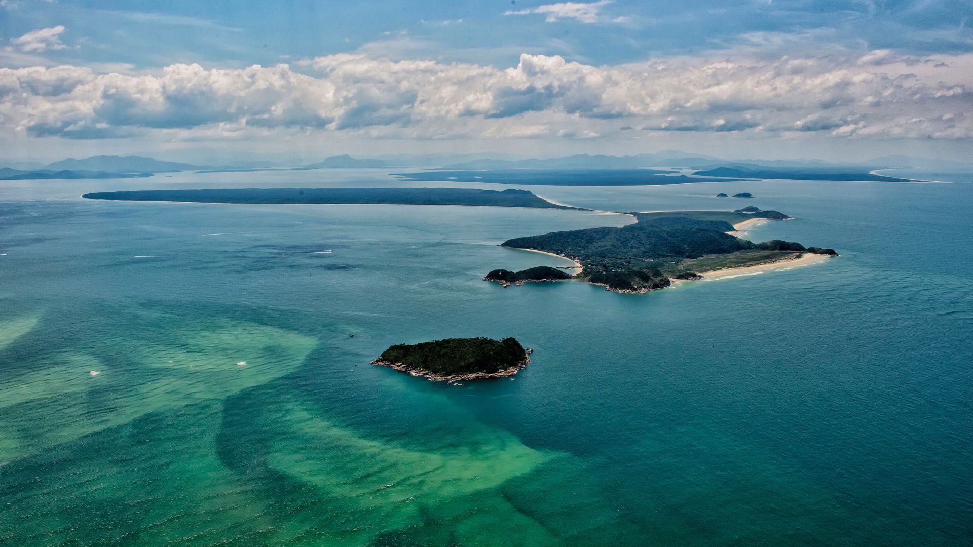 Vista aérea do litoral do Paraná, com ilhas, áreas de preservação ambiental e águas costeiras, região impactada por projetos ambientais financiados pela indenização da Petrobras