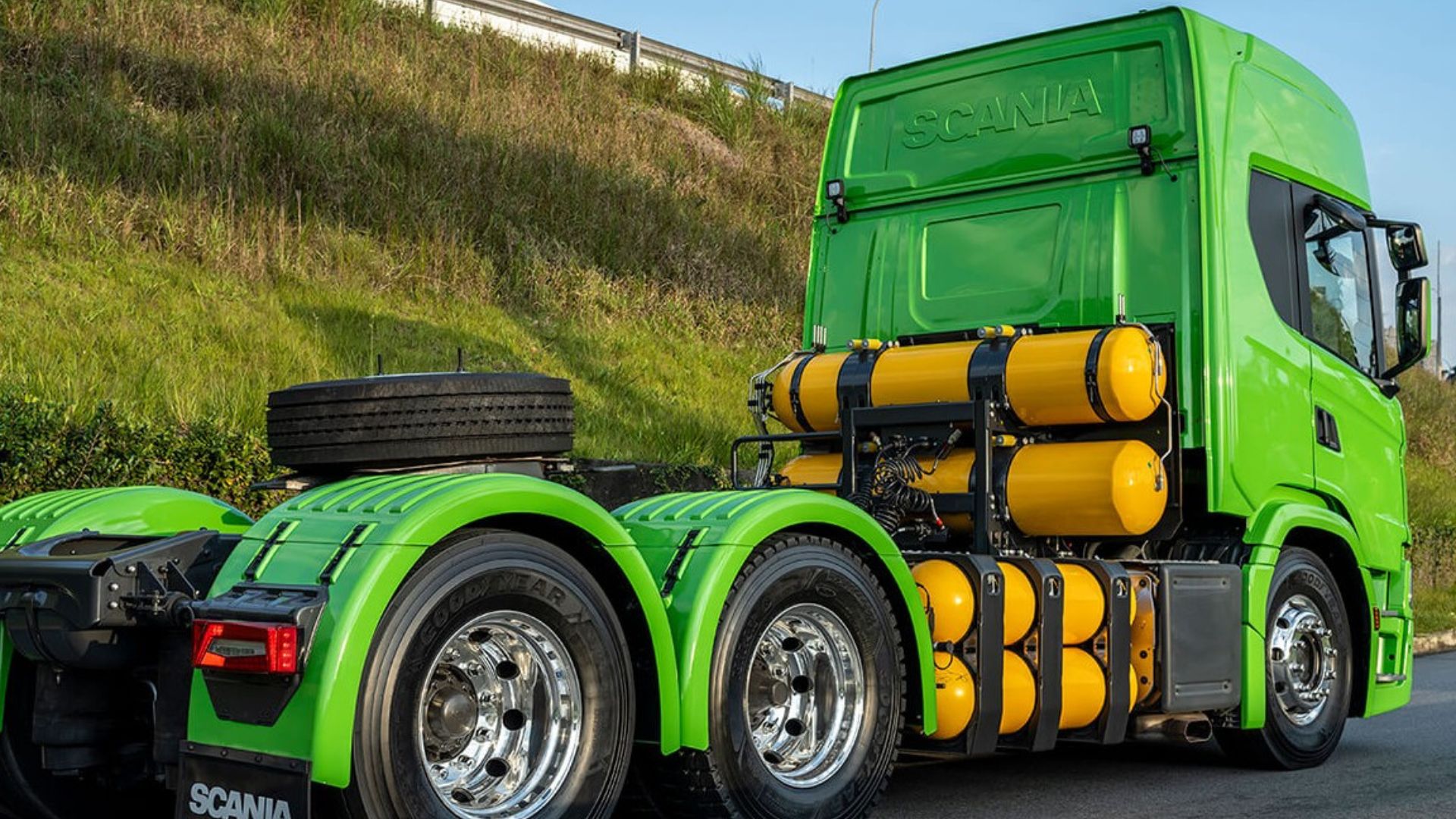 Caminhão Scania verde movido a biometano, com cilindros de gás instalados no chassi, estacionado em rodovia cercada por área verde.