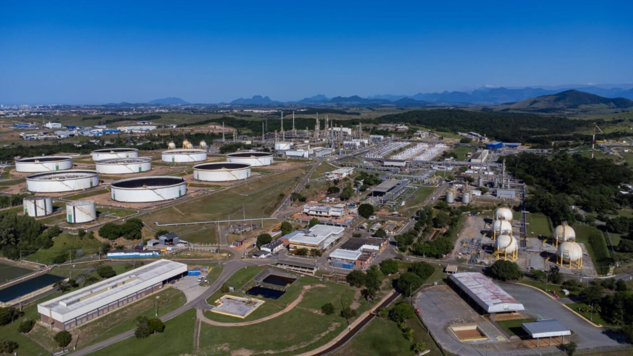 Vista aérea de un complejo industrial con tanques de almacenamiento y infraestructura de procesamiento, rodeado de vegetación y montañas al fondo.