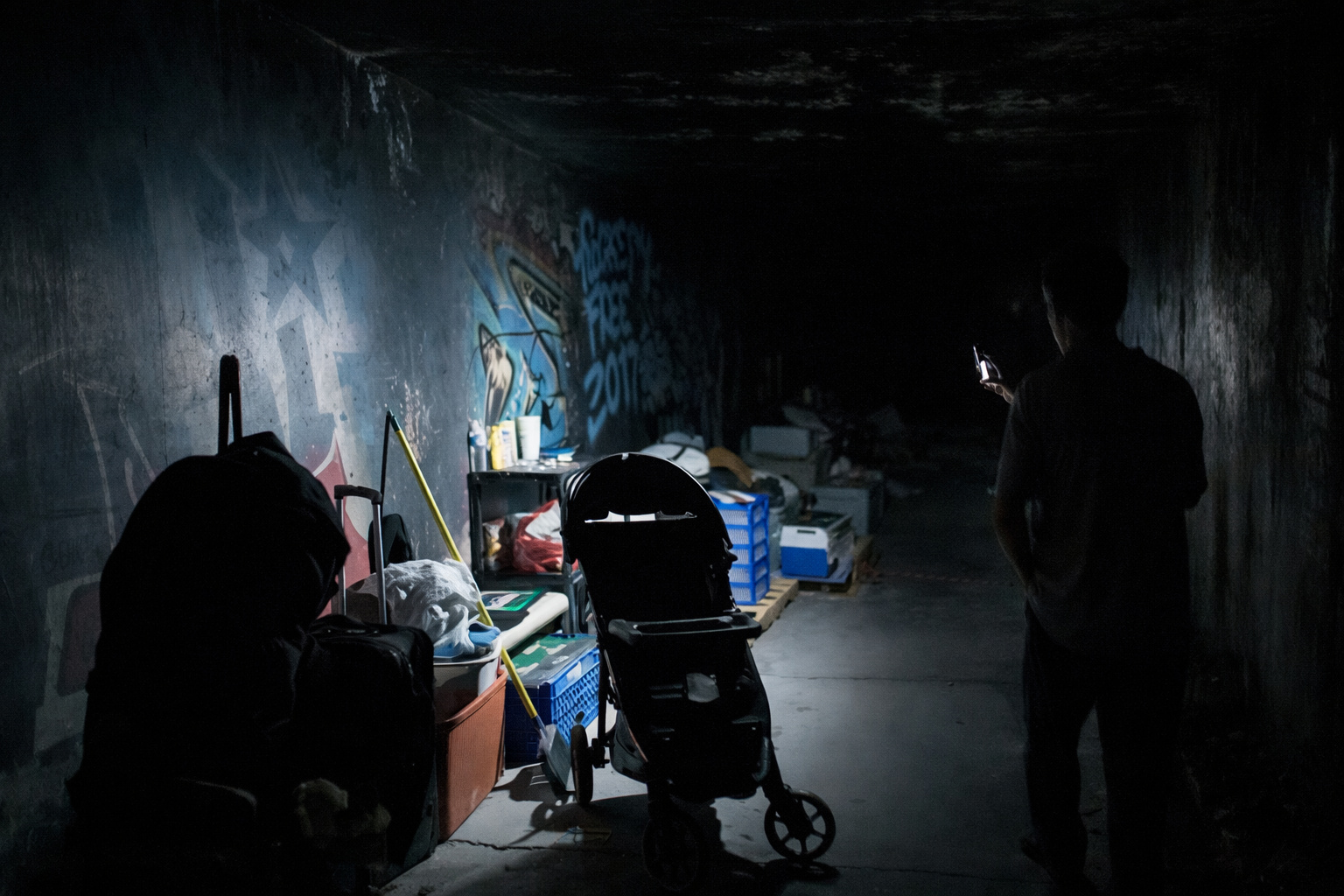 Interior de túnel de drenagem urbano sob Las Vegas, com carrinho, caixas, objetos pessoais e iluminação limitada, mostrando espaço ocupado como abrigo improvisado.