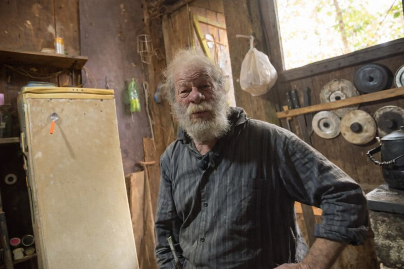 Homem idoso em ambiente rústico prepara alimentos em cozinha simples montada no chão dentro de casa