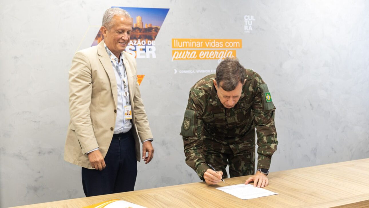Oficial del Ejército Brasileño firma documento al lado de representante de Copel durante ceremonia de asociación para proyectos de eficiencia energética y energía solar.
