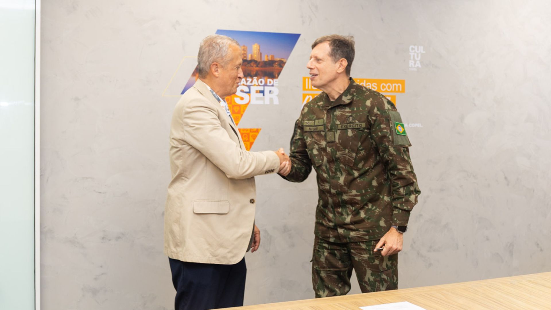 Representante da Copel e oficial do Exército Brasileiro apertam as mãos durante assinatura de acordo de cooperação para eficiência energética e instalação de usinas solares.