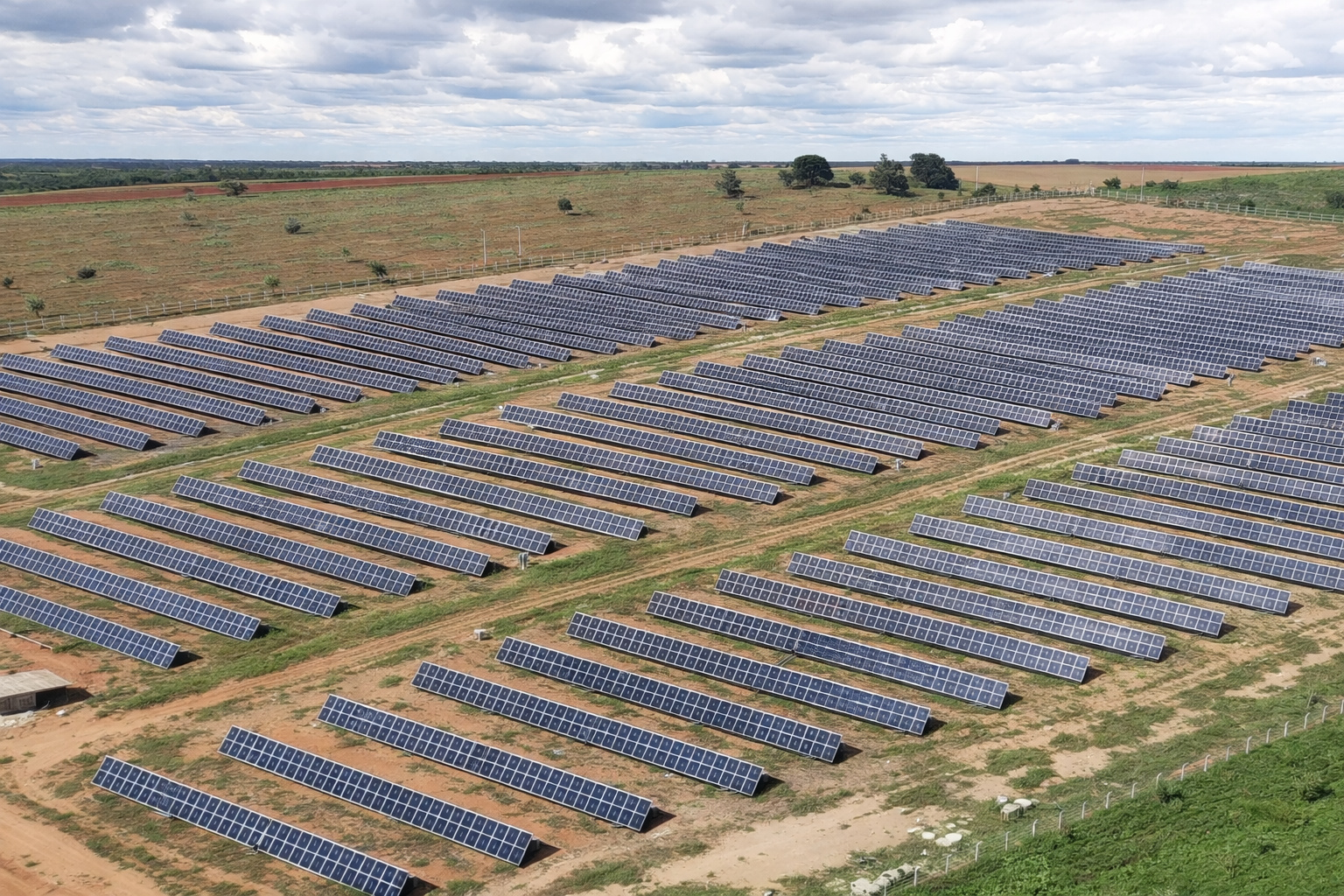 Vista aérea de usina solar com painéis fotovoltaicos em área rural sob céu parcialmente nublado.
