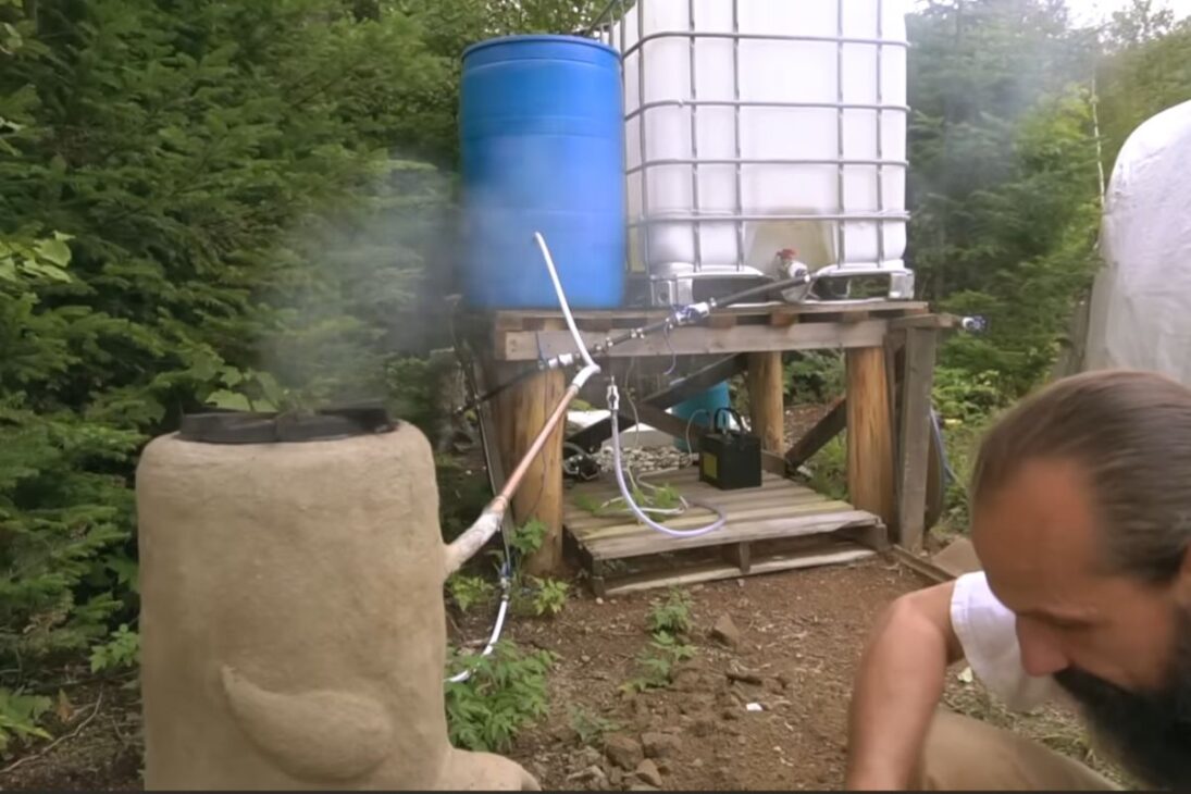 Calentador de agua fuera de la red en Quebec utiliza estufa cohete, barril elevado, tubos de cobre y termostato para calentar baño sin propano, bomba o electricidad, priorizando autonomía, eficiencia y atención a la seguridad en el uso diario.