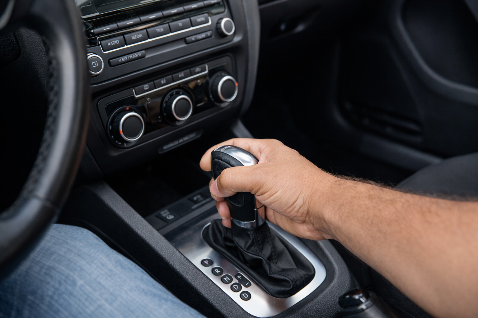 Mão de motorista segurando o câmbio automático dentro do carro, com seletor de marchas P, R, N e D visível no console central.