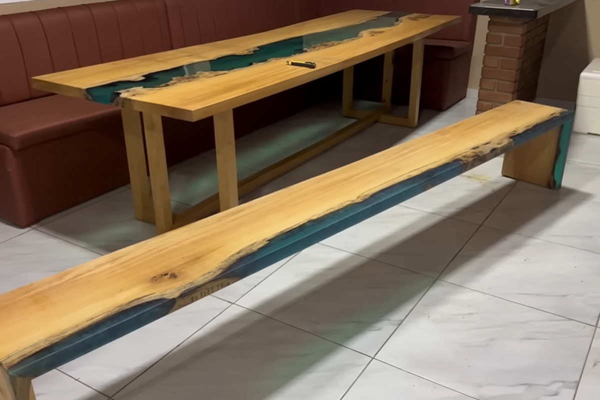Banco artesanal de madeira maciça com resina epóxi verde ao lado de mesa do mesmo estilo, resultado de projeto de marcenaria feito como continuação de uma mesa anterior.
